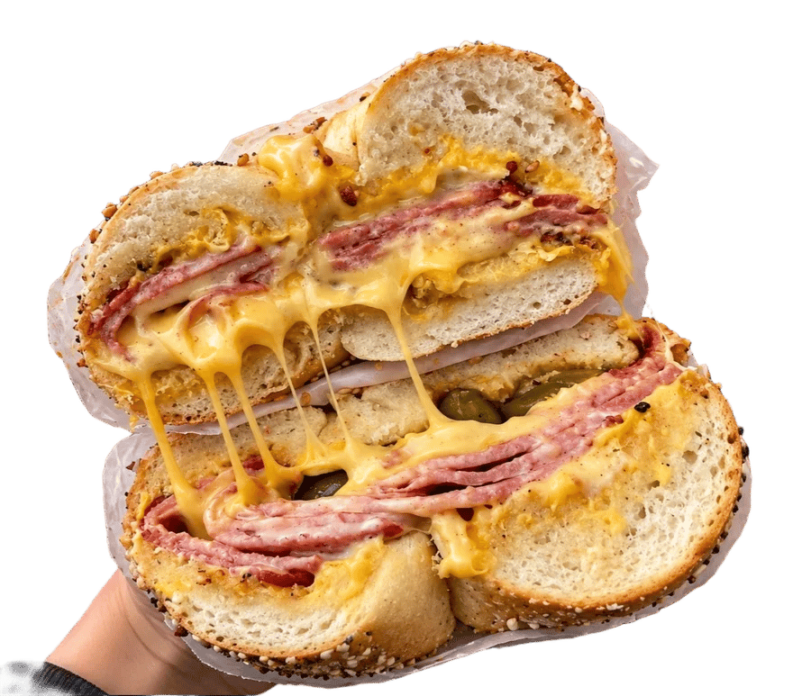 A bagel sandwich cut in half, stacked with deli meat and dripping melted cheese
